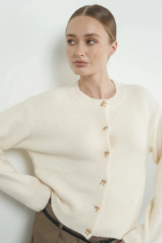 Soft white cardigan featuring beautiful gold bows for button closures, perfect for the holiday months.