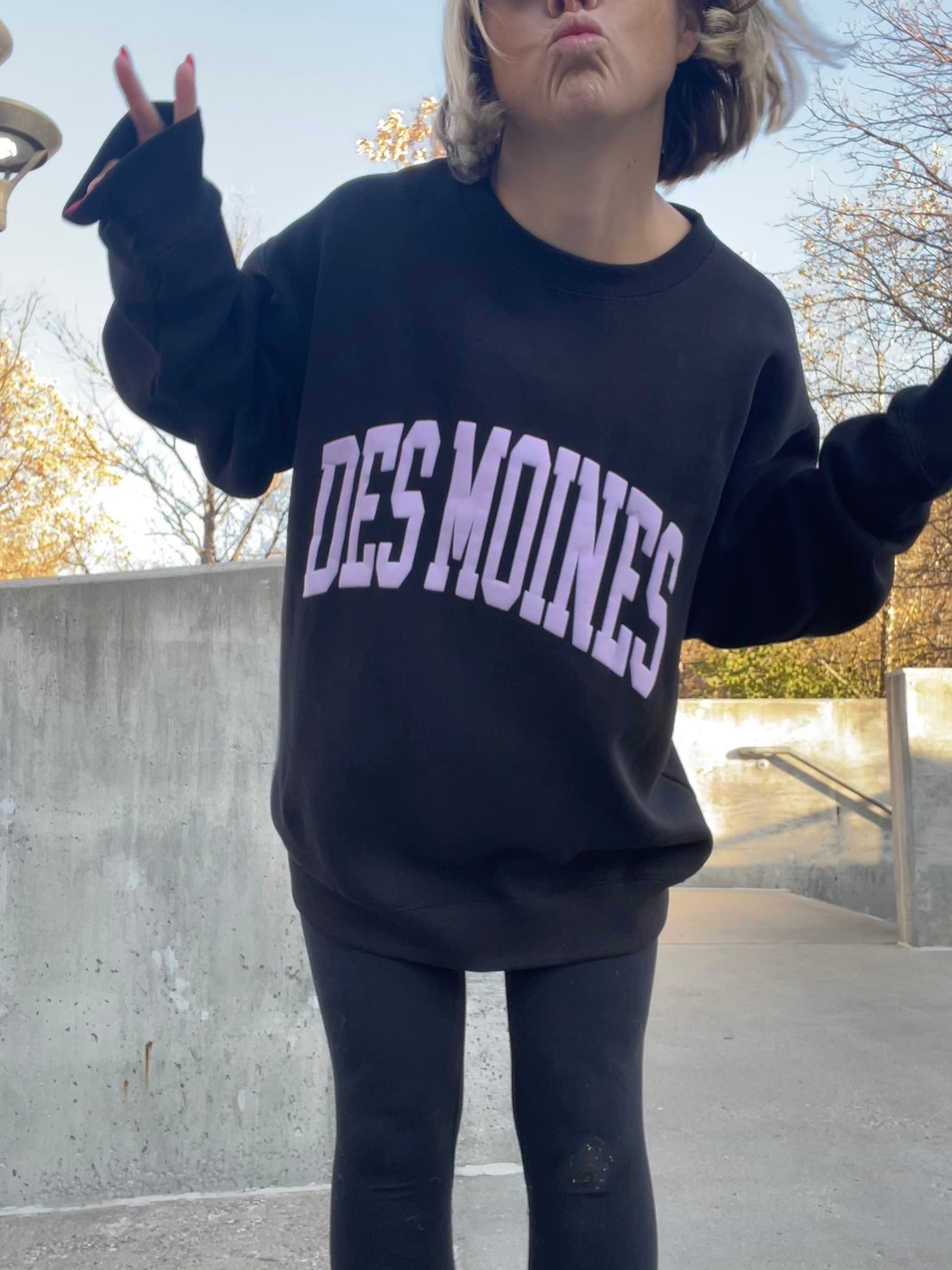 Oversized black crewneck sweatshirt with "DES MOINES" spelled in light purple puff print. 