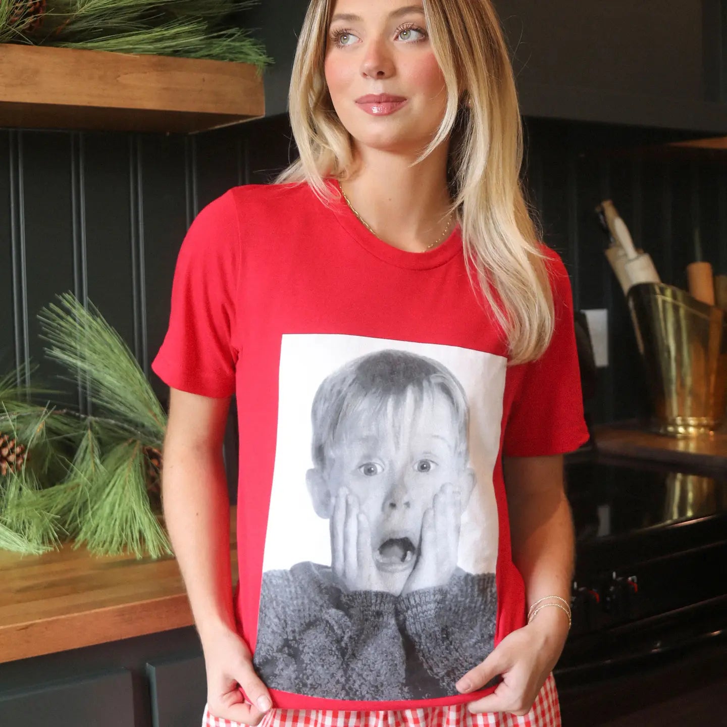 home alone holiday tee featuring a large black and white photo of kevin McCallister with his hands on his cheeks in his classic pose printed on a plain red tee.